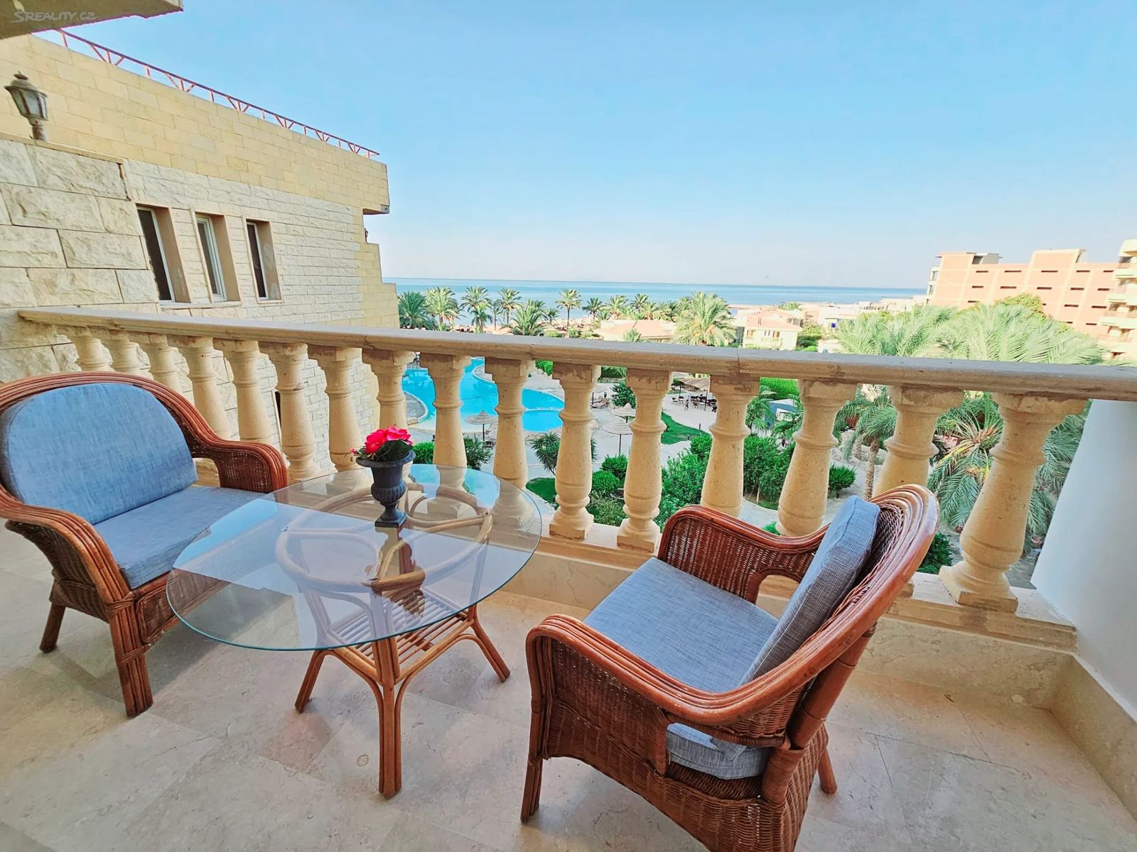 Balkon s ratanovými křesly a výhledem na bazén a moře