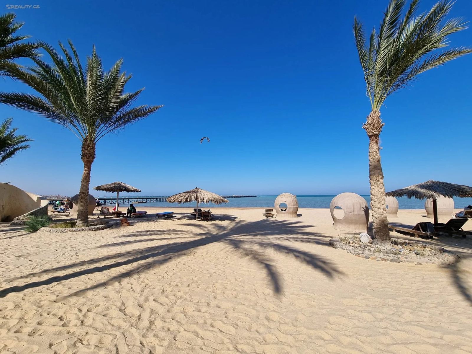 Písečná pláž s palmami, molem a kitesurfařem